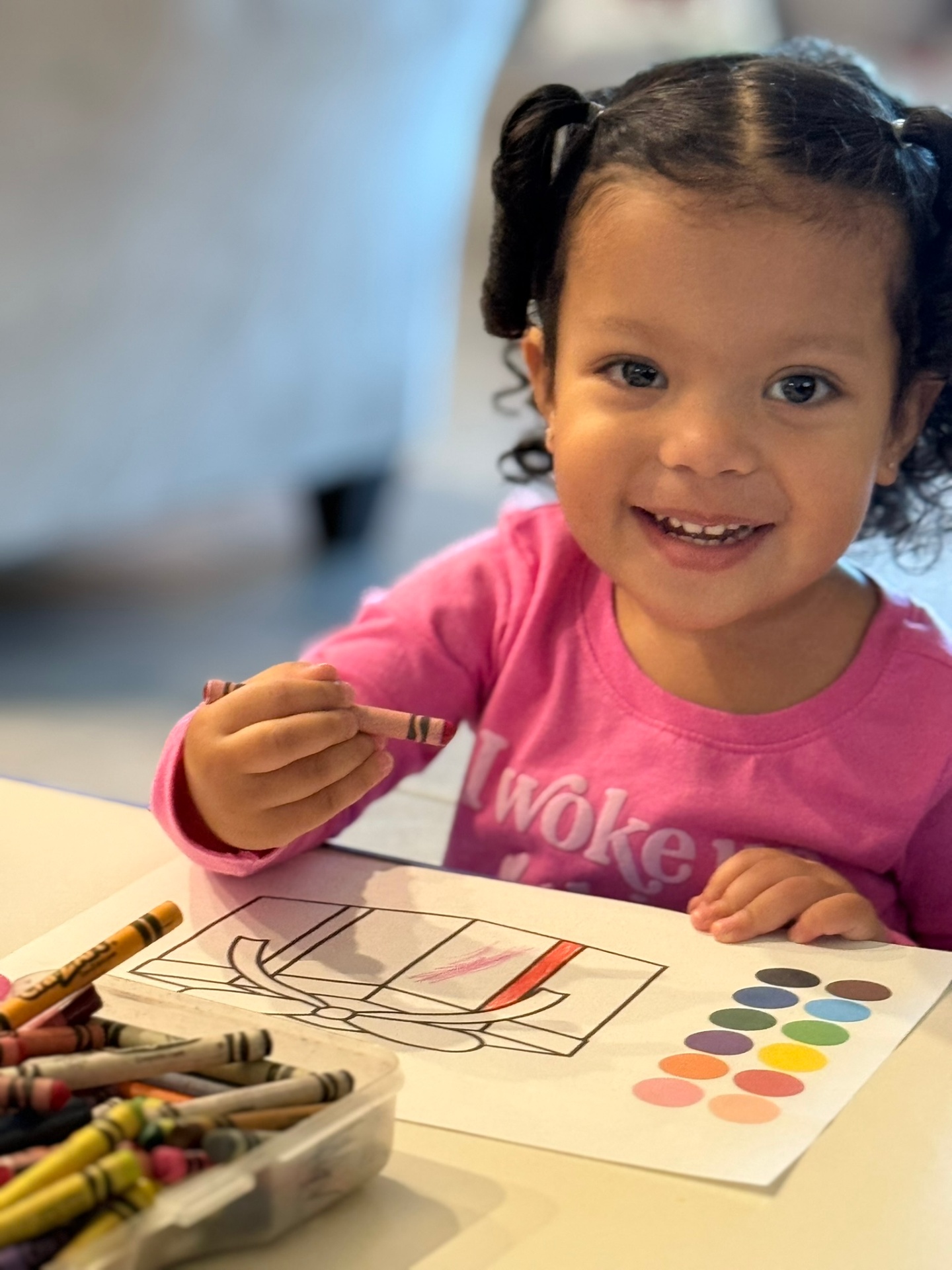 Smiling toddler in a pink shirt coloring with crayons