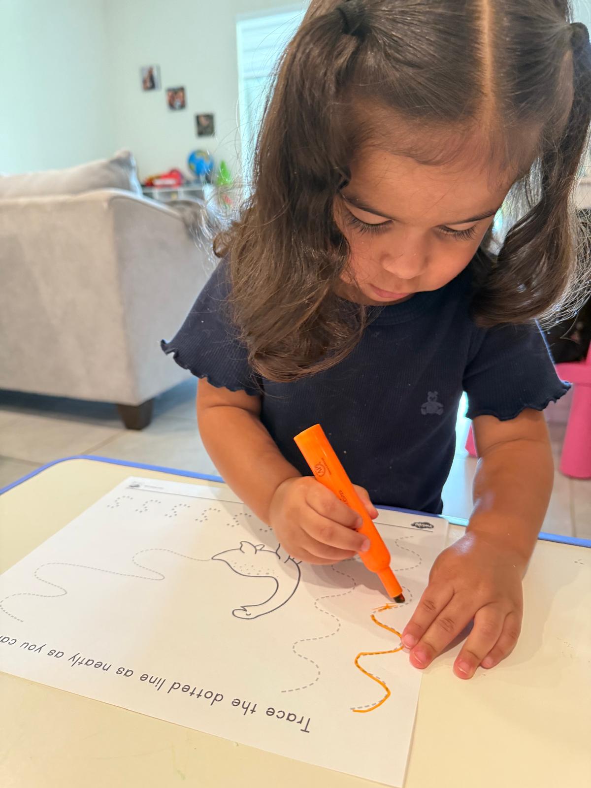 Focused toddler tracing dotted lines with an orange marker