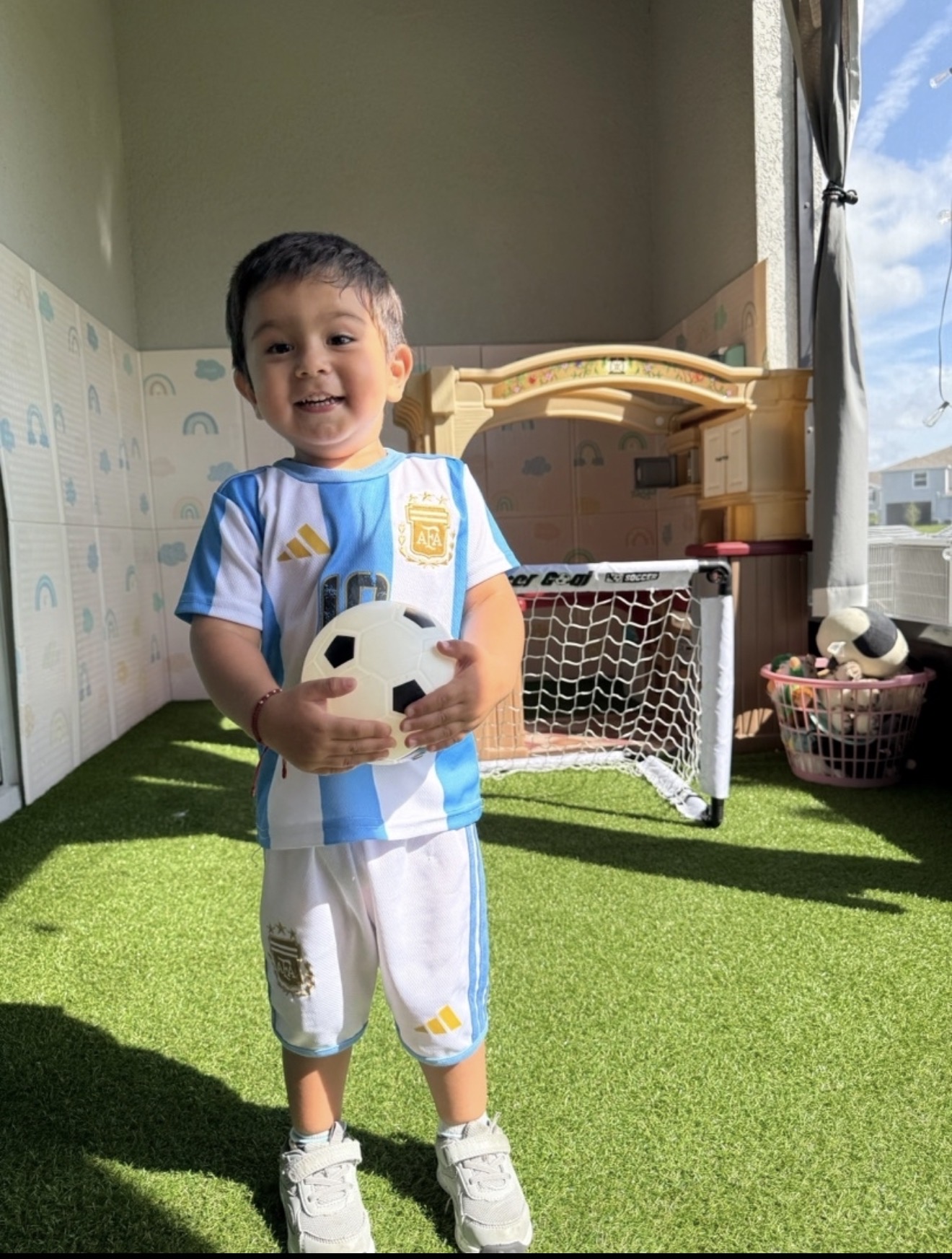 Smiling toddler in an Argentina soccer jersey holding a soccer ball