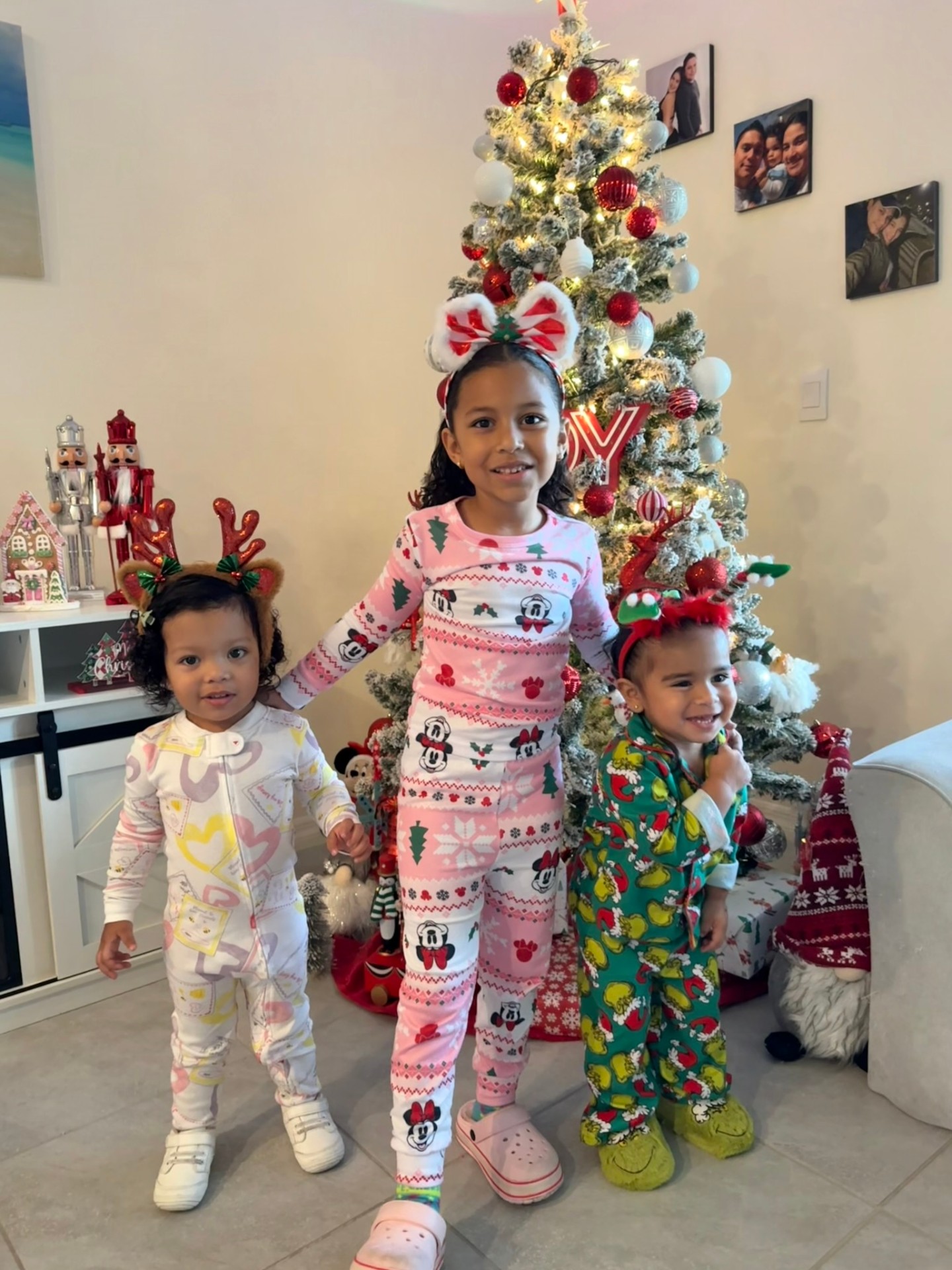 Three children in festive pajamas posing in front of a Christmas tree