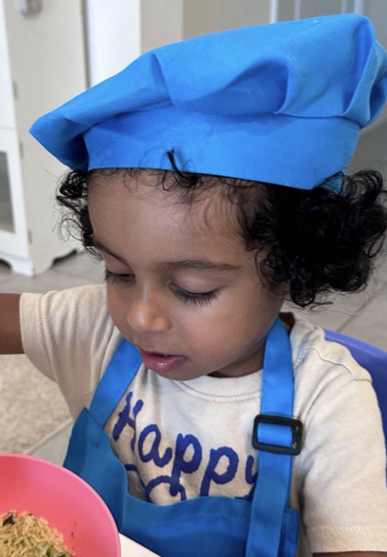 Toddler in a blue chef hat and apron cooking in the classroom kitchen