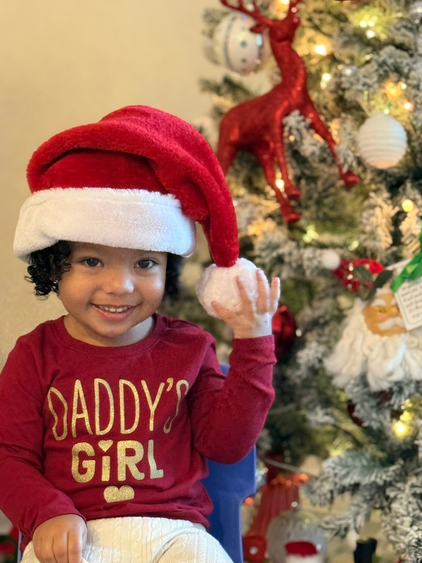 Smiling toddler in a Santa hat next to a decorated Christmas tree
