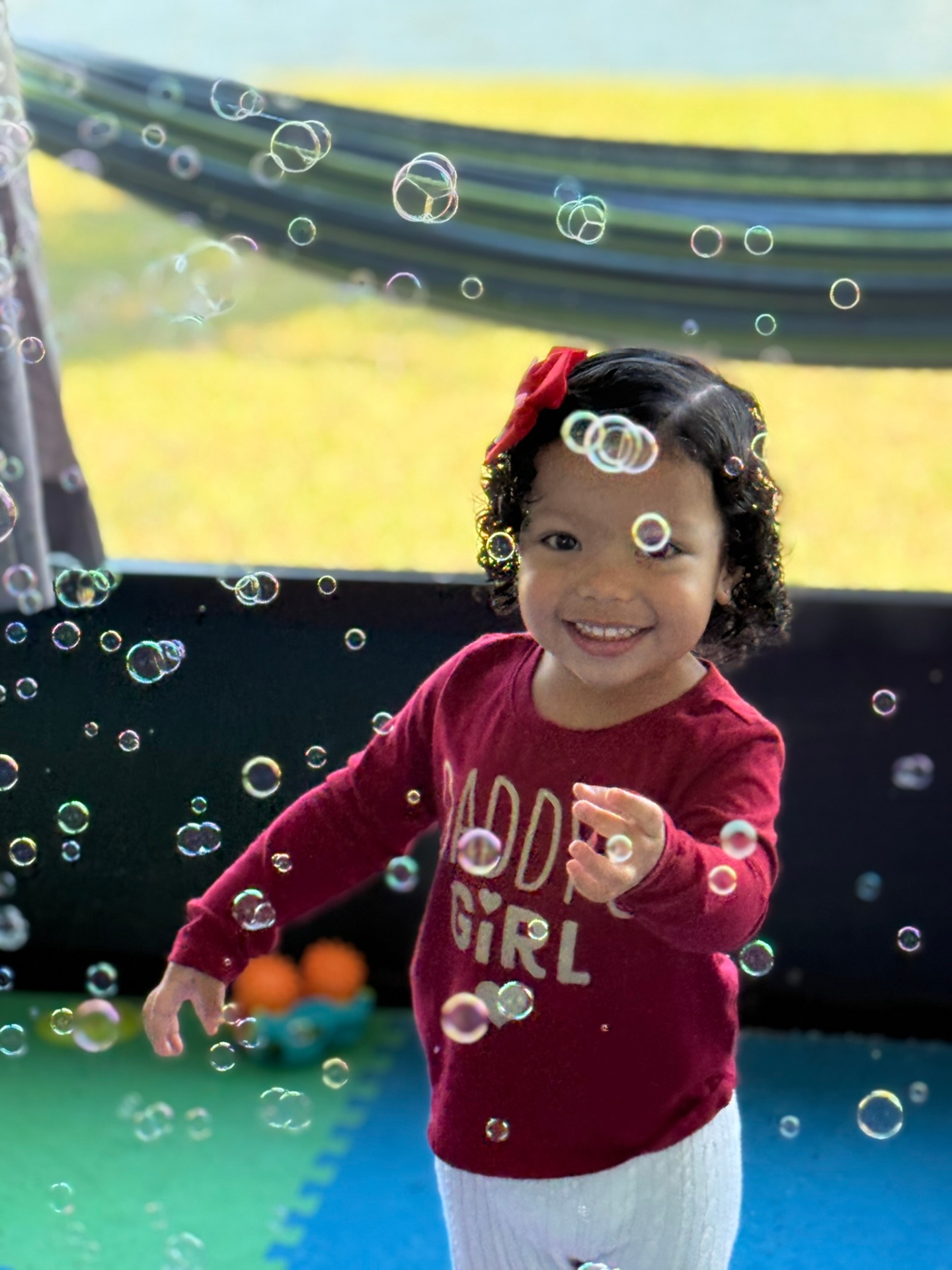 Smiling toddler in a red shirt playing surrounded by soap bubbles