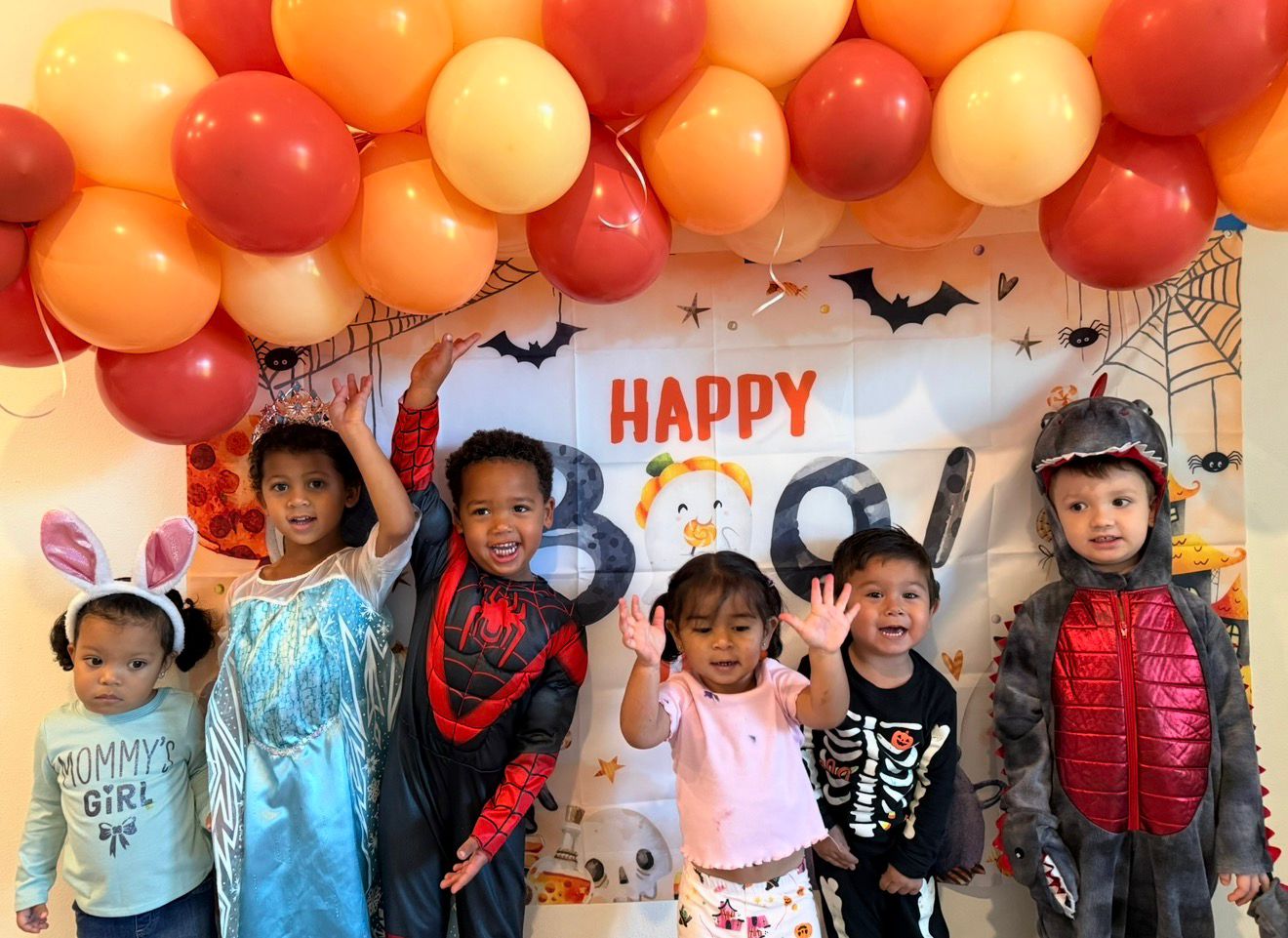 Children in Halloween costumes posing in front of a Happy Boo backdrop